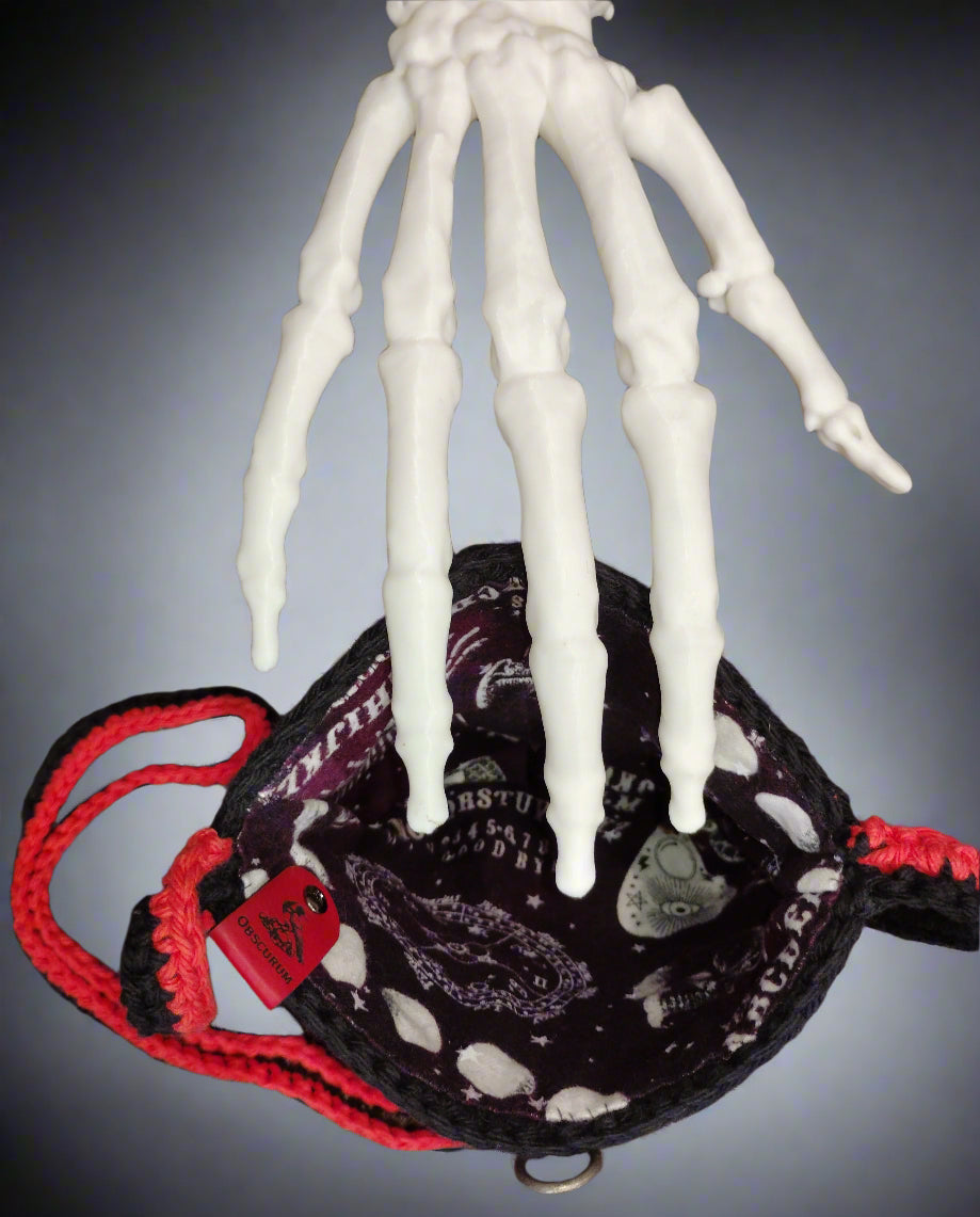 White skeleton hand holding a black bag with red strap on a gray background