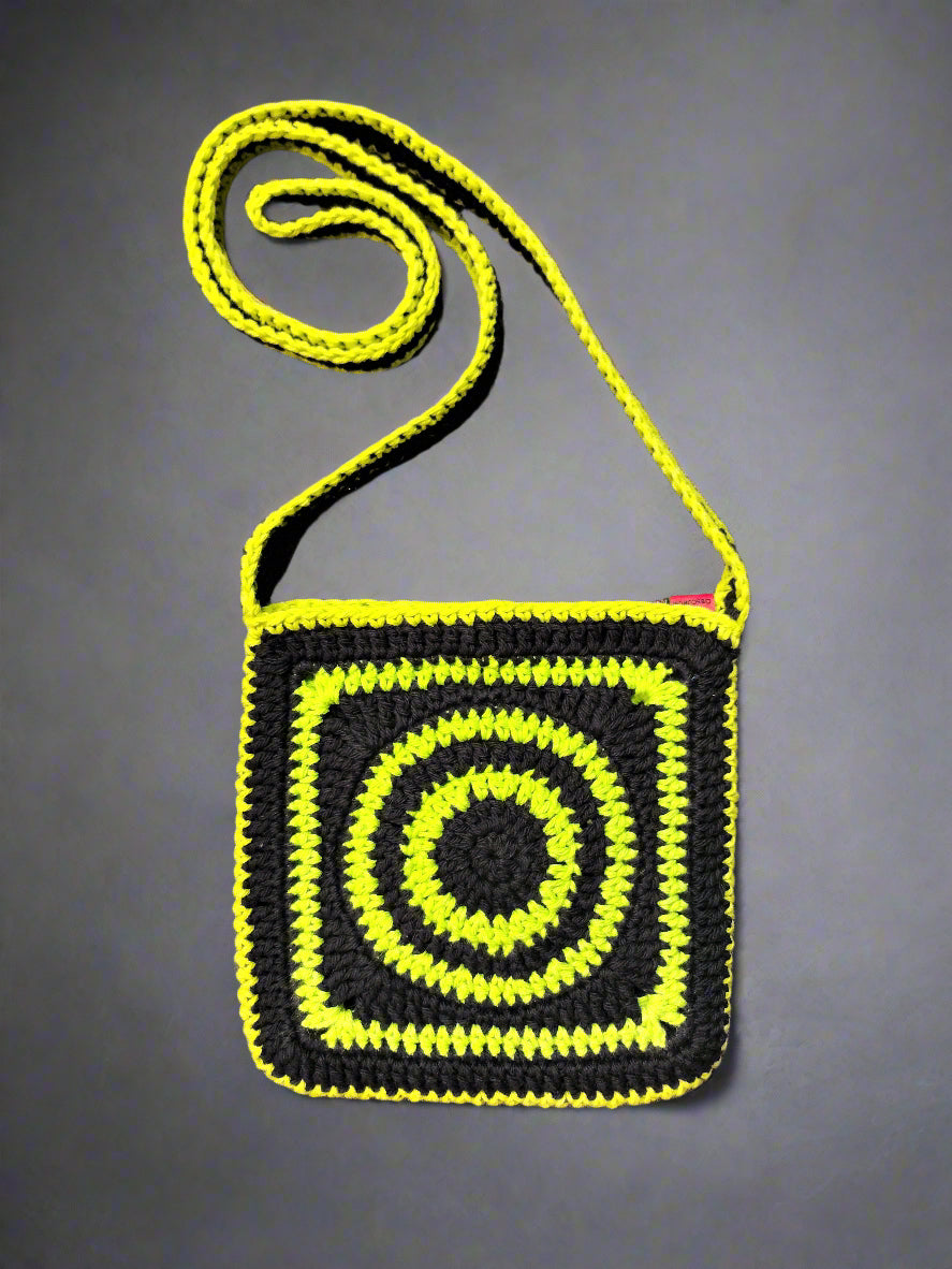 Crocheted bag with yellow strap and black square design on a gray background